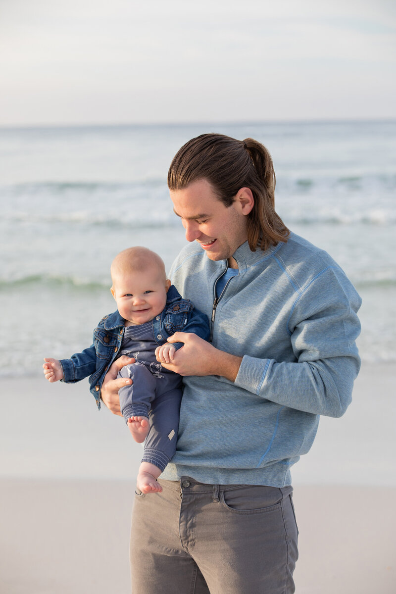 A dad holding a smiling baby at the beach