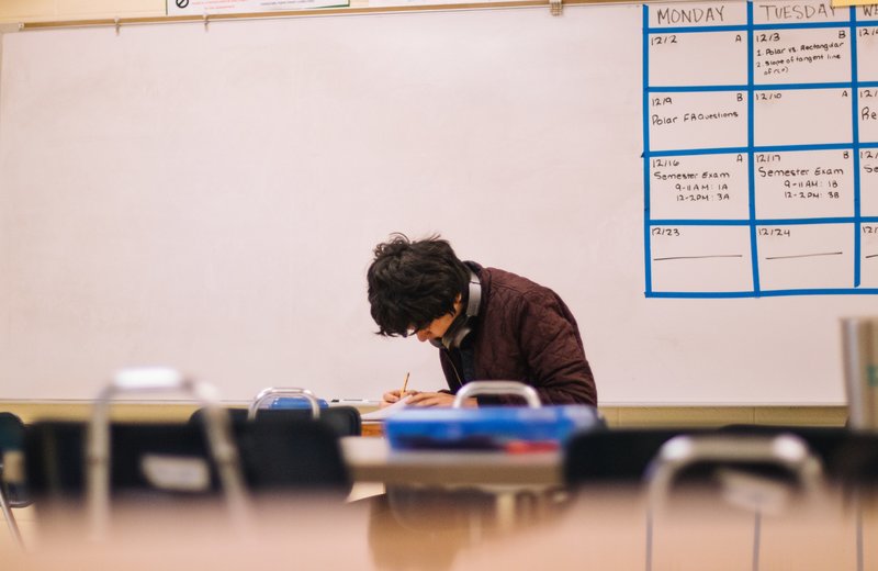 student sitting inside a classroom writing with a pencil