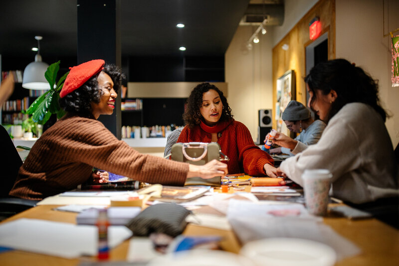 3 Black women sitting at a table working on their art collages