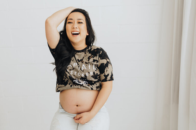 Woman laughs as she shows her pregnant belly during a maternity session