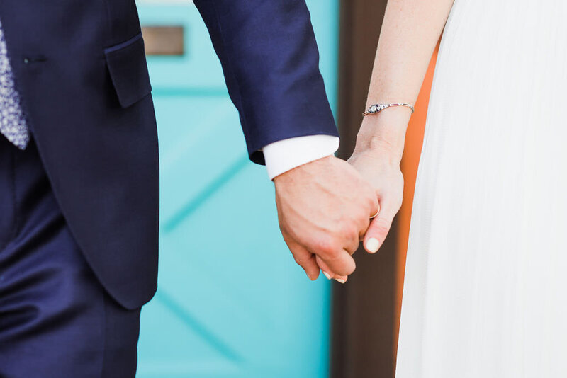 Close up of bride and groom holding hands in front of turquoise door on their wedding day