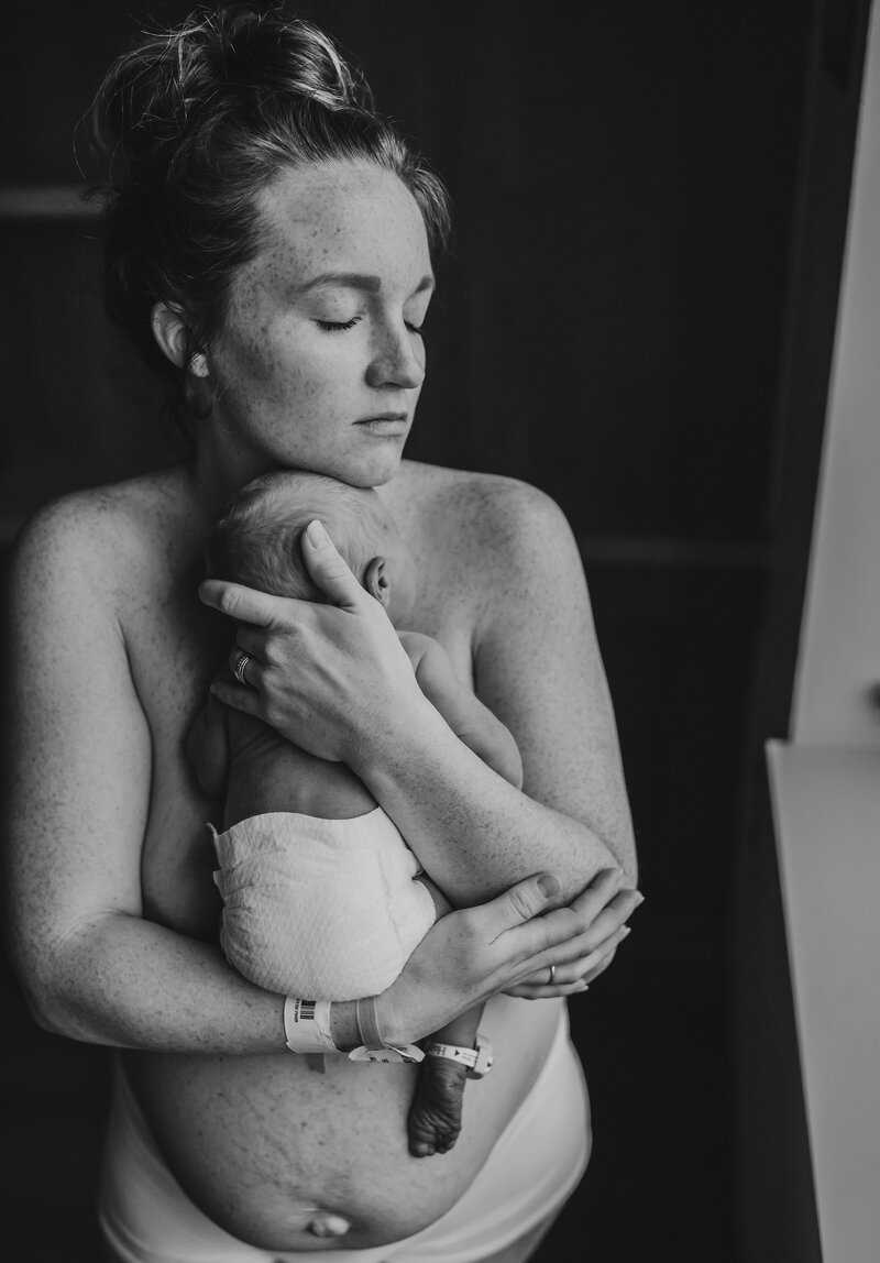 Black and white family photo of mother holding newborn baby close to her
