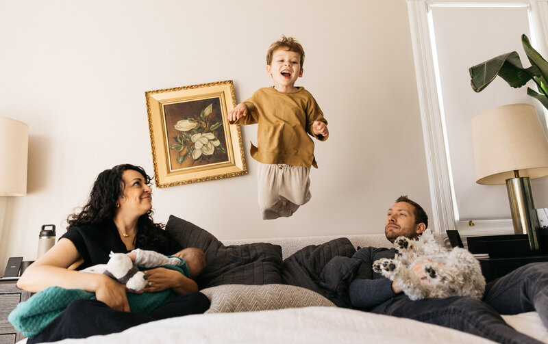 mother, father, infant son, and toddler son jumping on the bed during a photo session at home in san francisco.