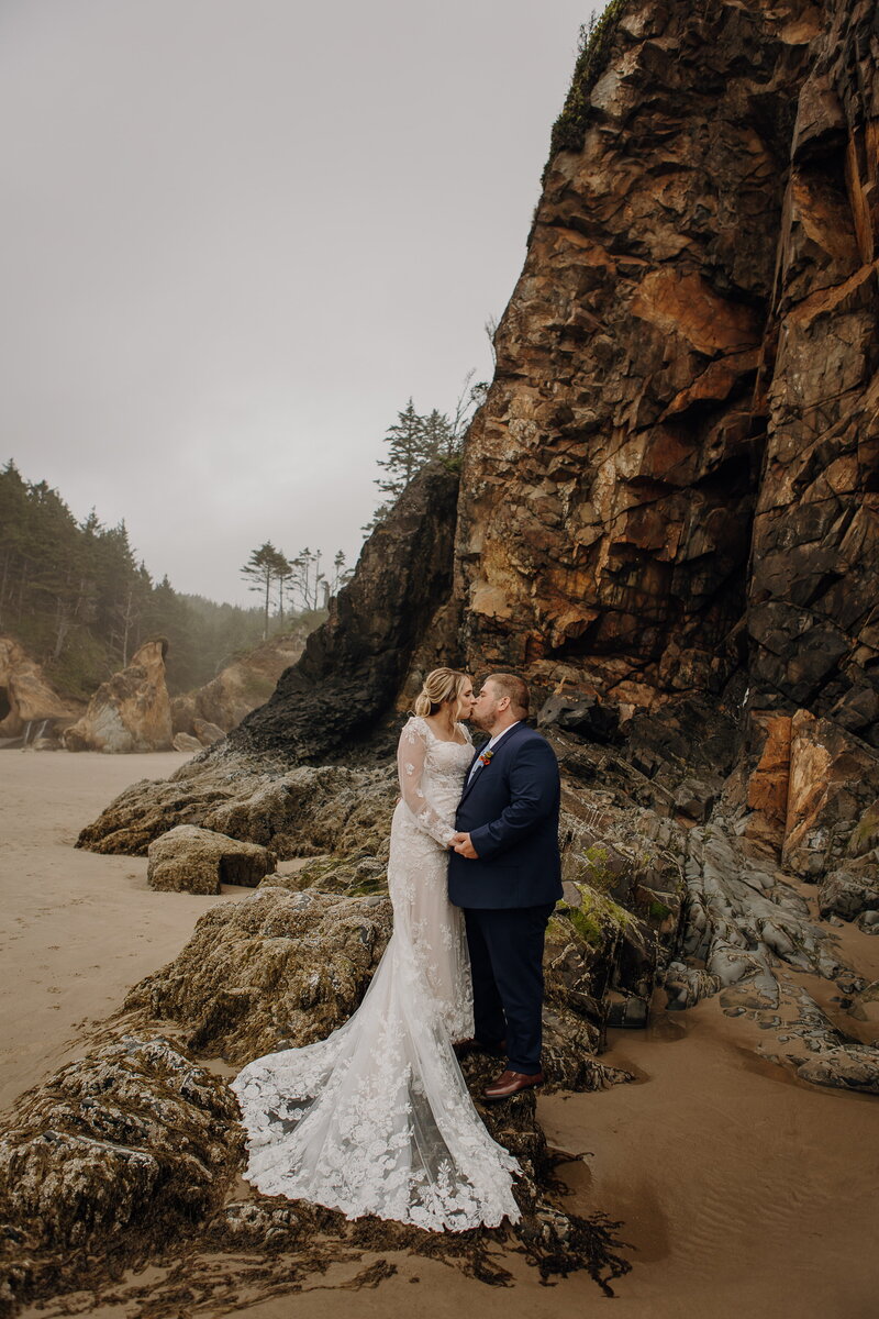 a mand and woman in wedding attire stand on the rocky beach shores of Yachats in Oregon