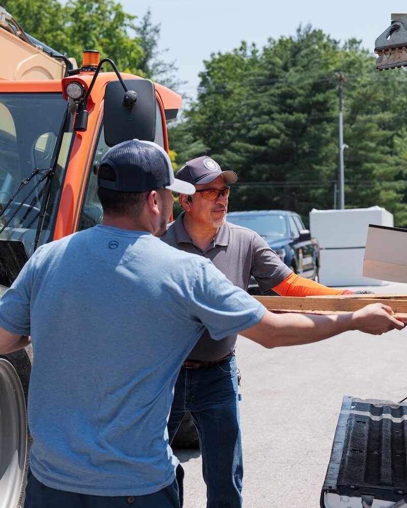 Members of the Royco Roofing team are working together to remove a piece of wood from the back of a truck