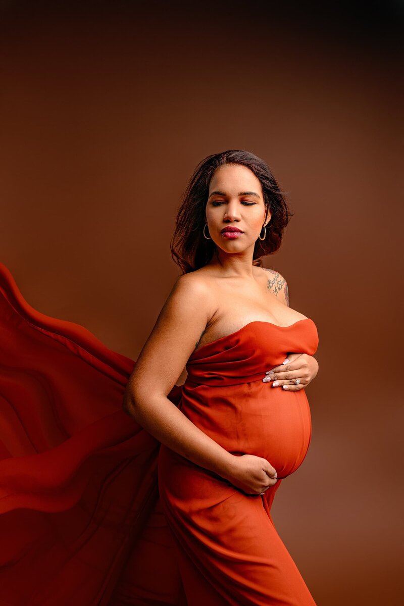 Charlotte expectant mom is posed with both hands on her belly wrapped in a rust colored silk