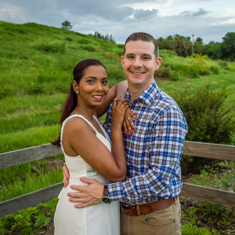 Engaged couple poses at a park in front of wooden fence