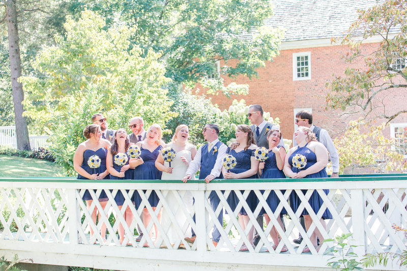 Bride, groom, and their bridal parties smile atop a white bridge holding bouquets