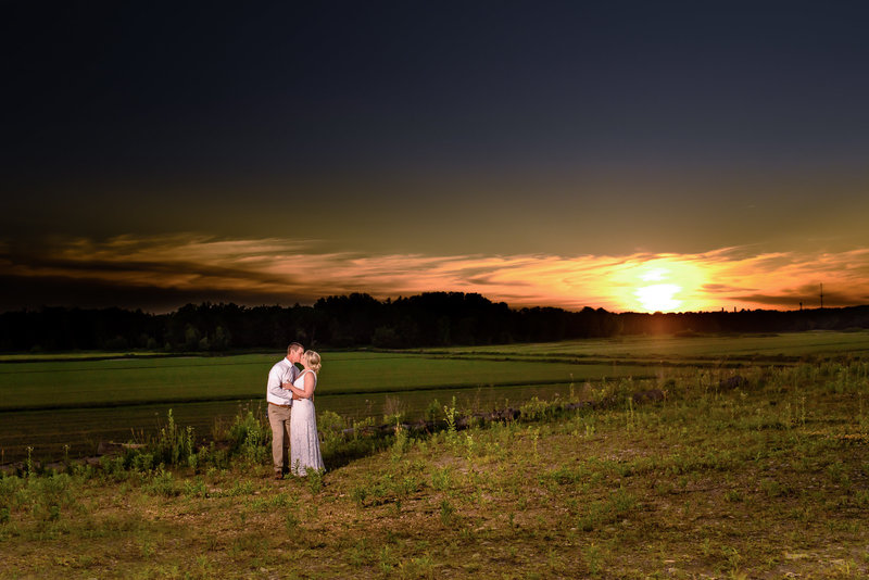 Bride and groom kiss overlooking fields during a sunset