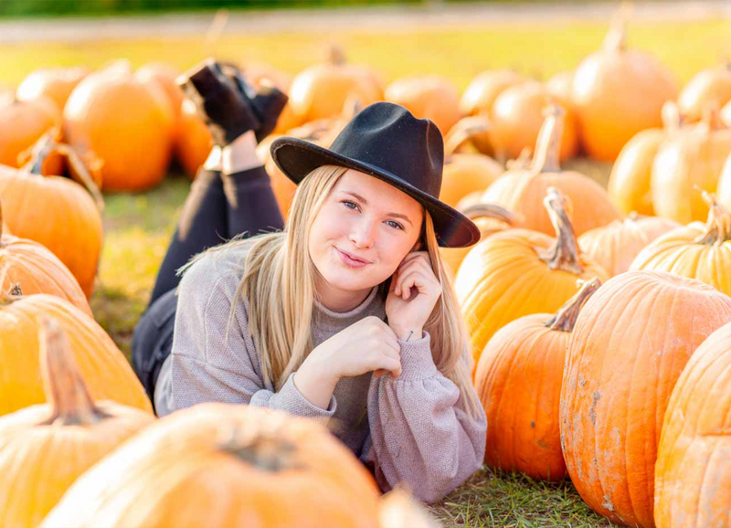 close up of high school senior girl wearing sweater and laying on stomach in a pumpkin patch