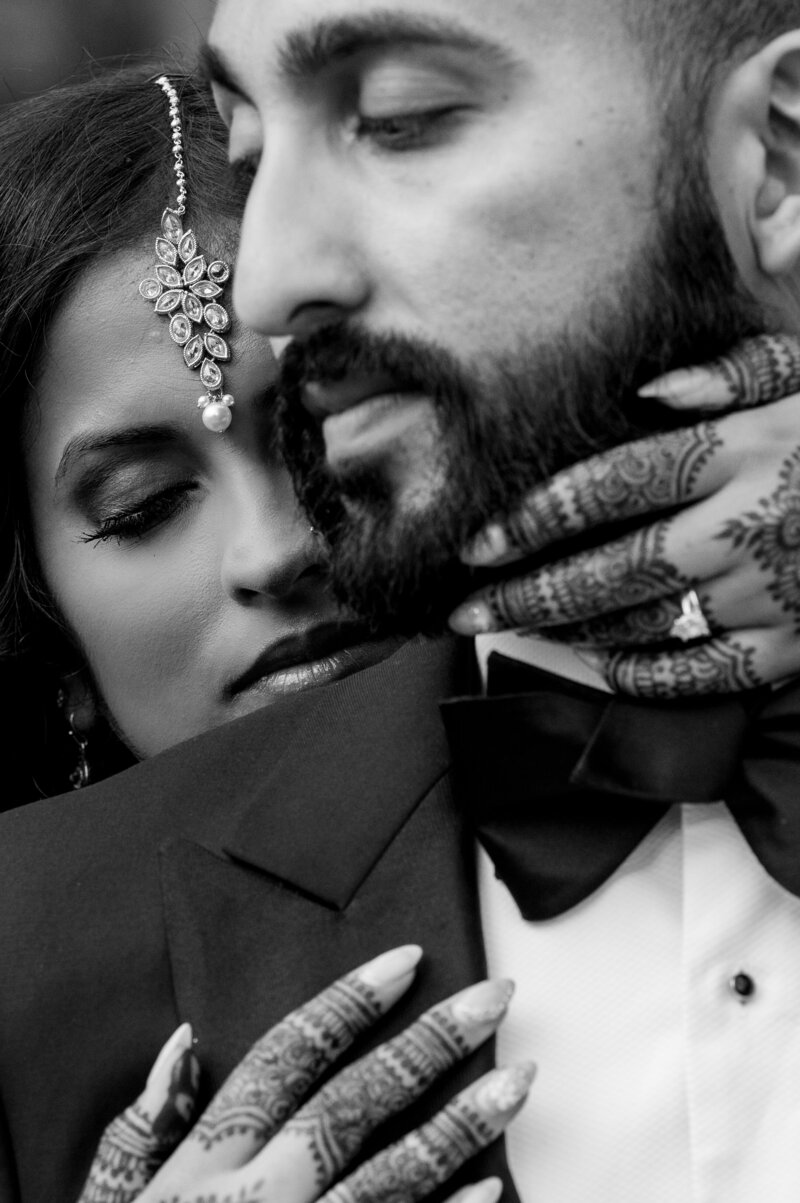 Black and white close-up of a bride with intricate henna tattoos and a teardrop forehead piece embracing a groom in a tuxedo at a Park Farm Winery wedding.