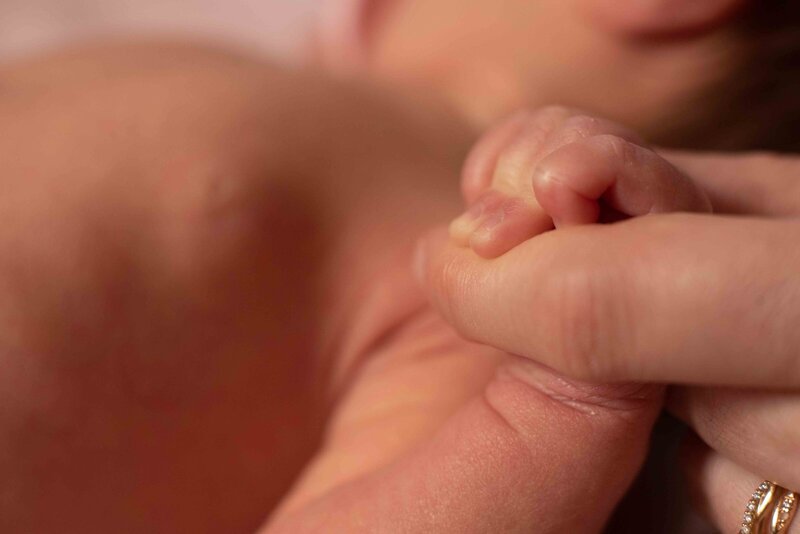 A mother's finger gripped by a newborn's hands