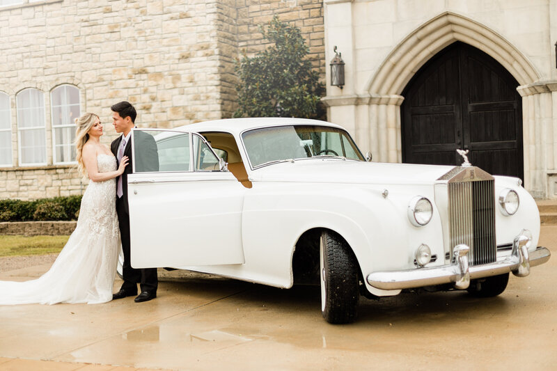 bride and groom standing outside castle venue next to a white Rolls Royce