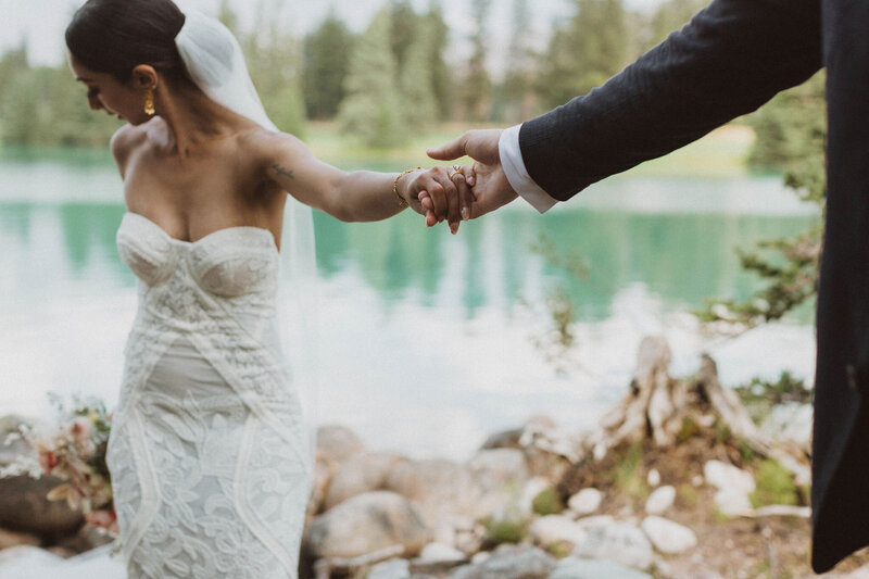 bride and groom holding hands by lake after elopement