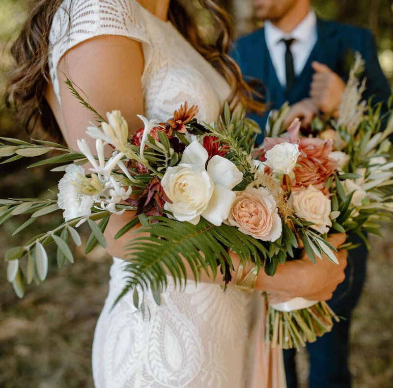 Bridal bouquet in woman's arms with roses and ferns and other flowers.