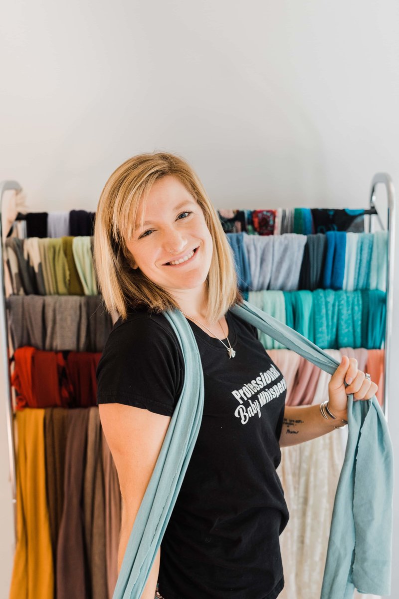 Kira Jeffrey posing in her portrait studio in front of colorful wraps for newborn portraits