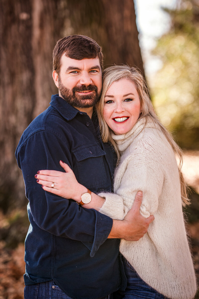 A couple is standing in front of a tree and smiling at their couple session in Newnan, GA.