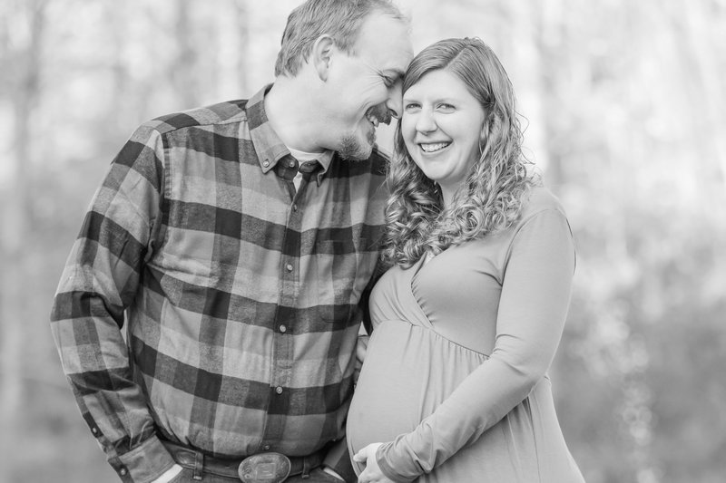 Husband and wife embrace and smile as wife hold her pregnant belly during maternity photo session