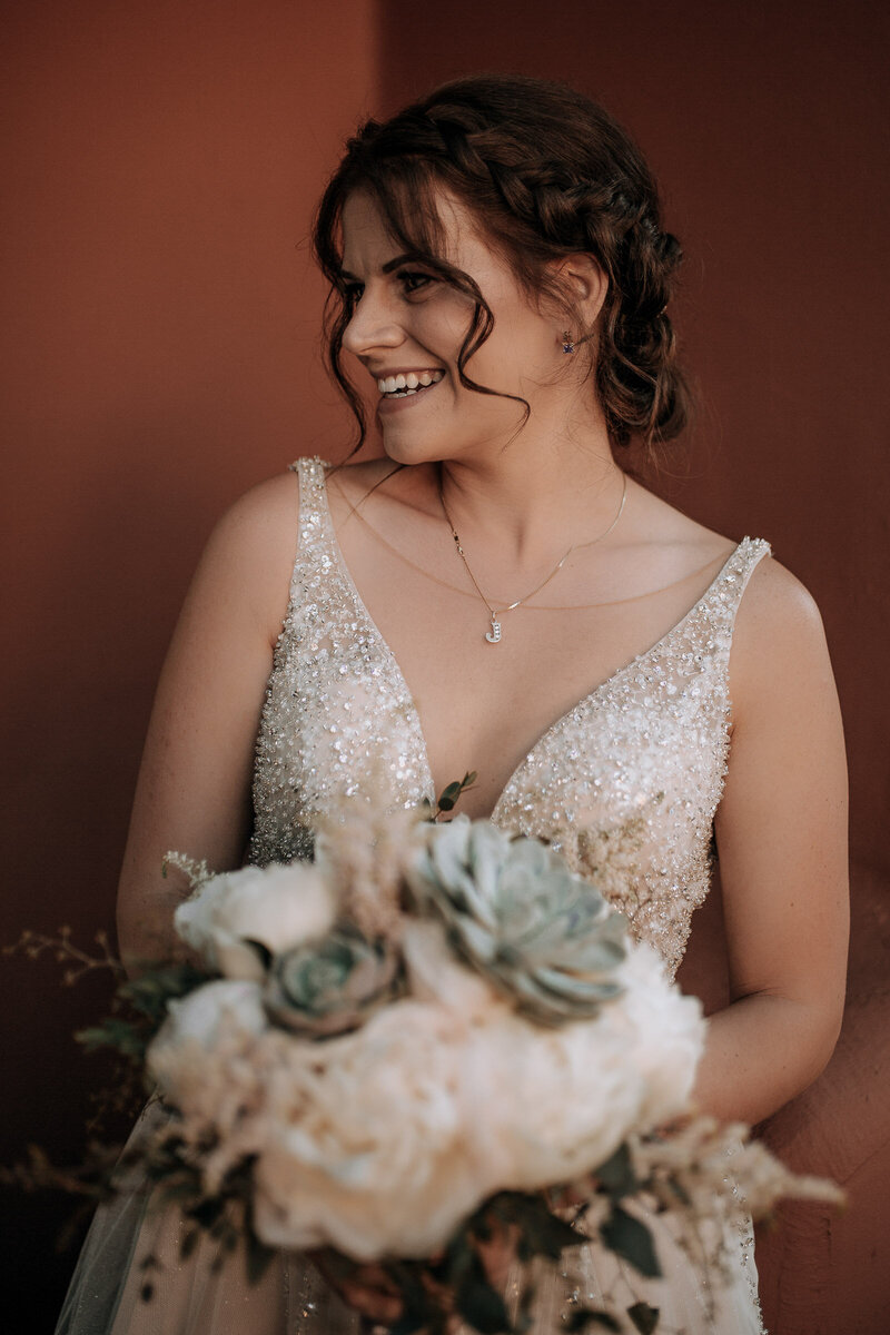 bride holding white bouquet with green succulents in sparkly sleeveless wedding dress with natural wedding makeup and messy bridal updo