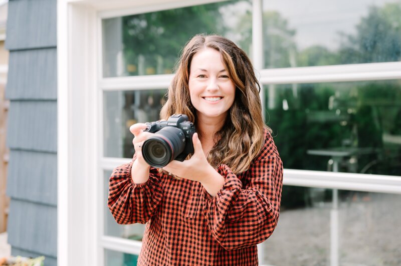 Kelli smiling in a red plaid shirt while holding a camera