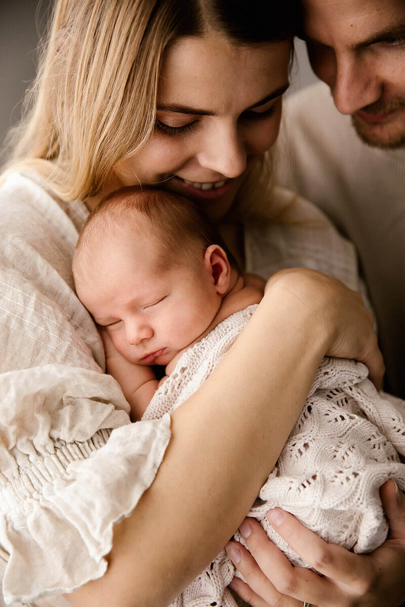 A mother holding her baby while her husband looks over her shoulder during a newborn photoshoot with new plymouth photographer aimee kelly photography