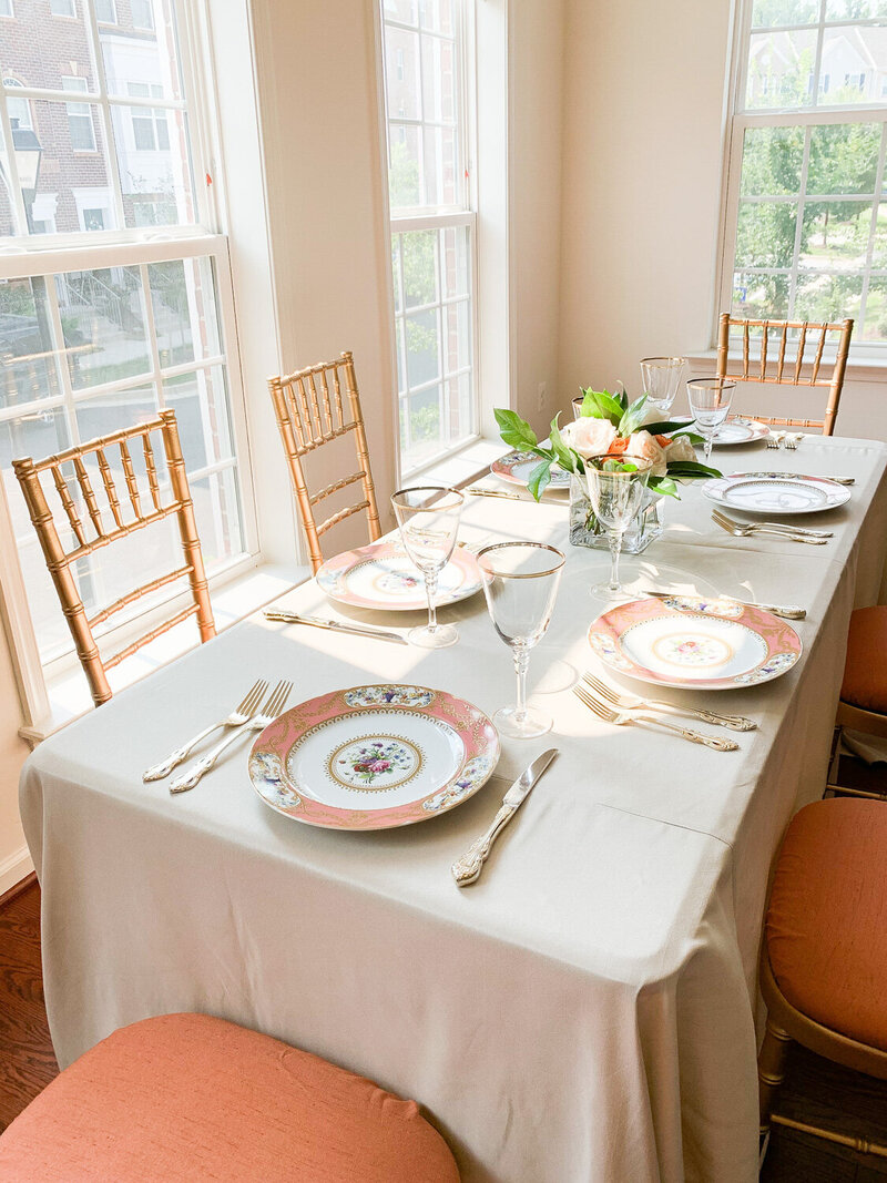Chairs, rectangular table with plates, utensils, glasses and a flower centerpiece on top