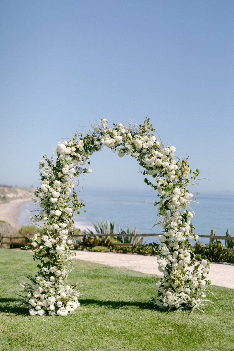 Lush white floral wedding arch overlooking the beach