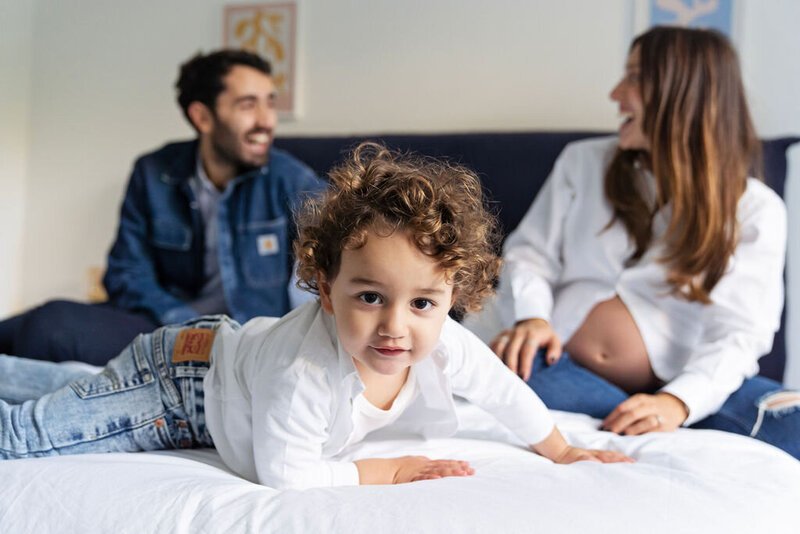 Little boy on bed with parents laughing in the background