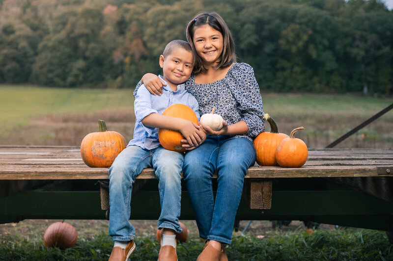Two siblings hugging sitting on a wagon with pumpkins