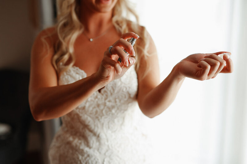 bride spraying perfume on her wrist during wedding day