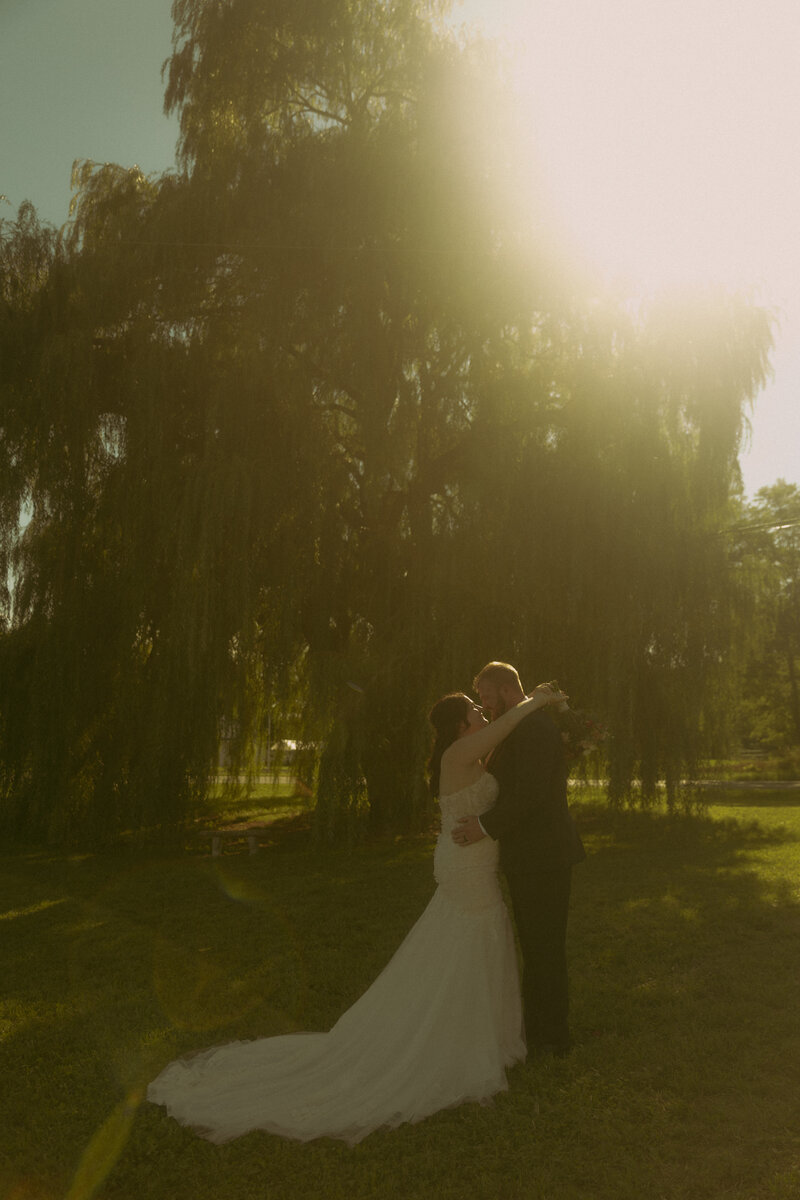 The mother of the bride prepares the veil for the bride as the sun shines through a window, offering a beautiful backlight effect