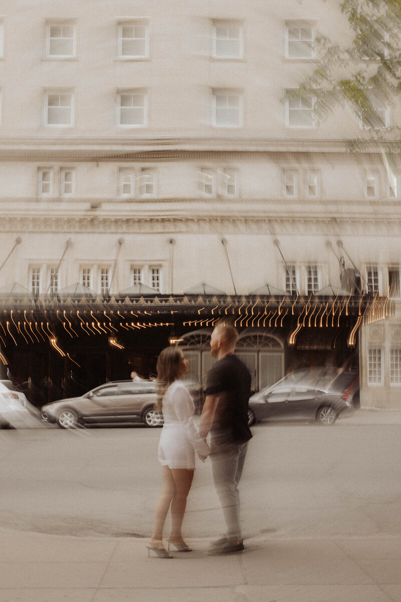 Motion-blurred image of a couple walking past a hotel entrance.