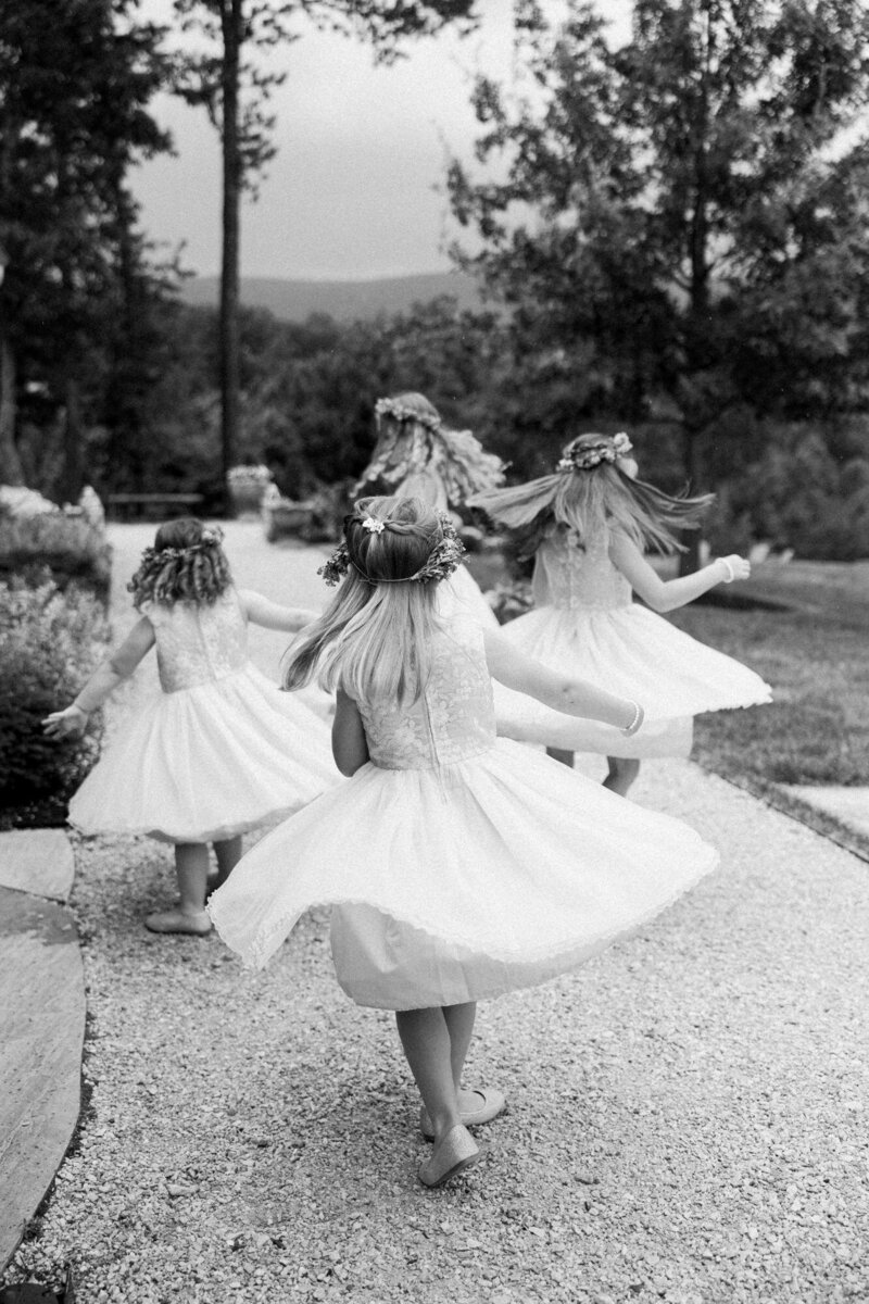 Young girls in white dresses and floral crowns, captured by a luxury wedding photographer, walking down a path.