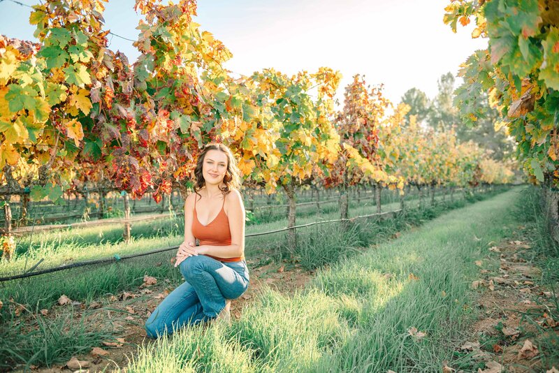 Girl in orange tank top and blue jeans in a fall vineyard