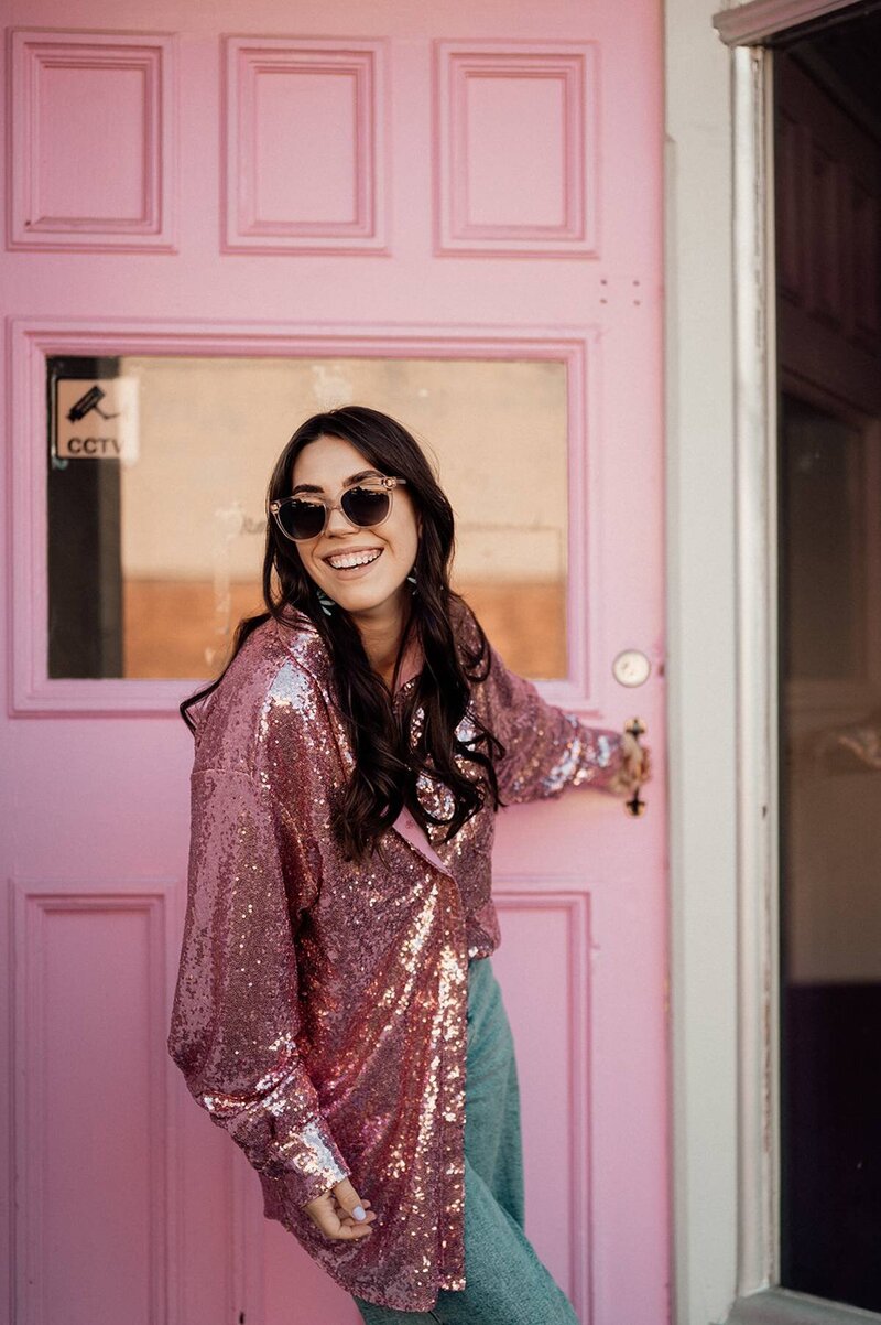 Branding portrait of Sharni, photographer laughing in front of a pink door during a lifestyle photography session.