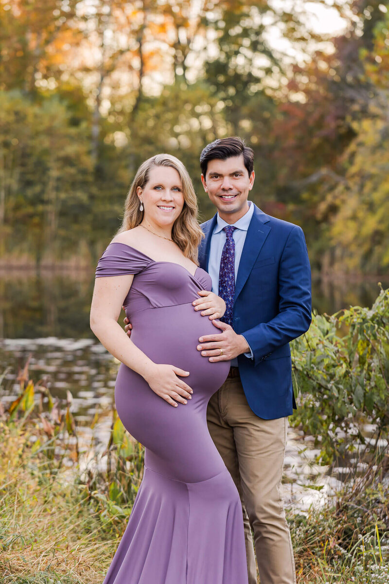 A well-dressed expecting couple posing in front of a pond in Northern Virginia.