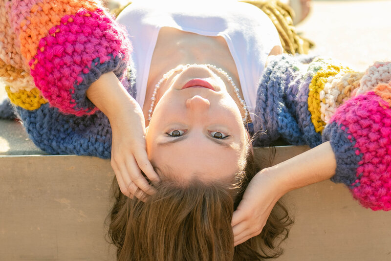 Senior portrait of a girl wearing a rainbow cardigan lying upside down
