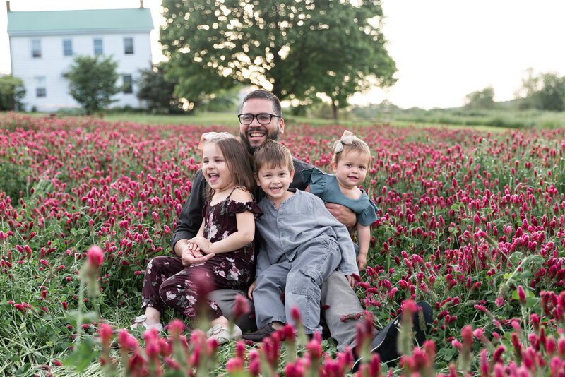 A father laughs and smiles with his children during their lifestyle family photos in a crimson clover field at the Miller's Farm in White Hall, Maryland