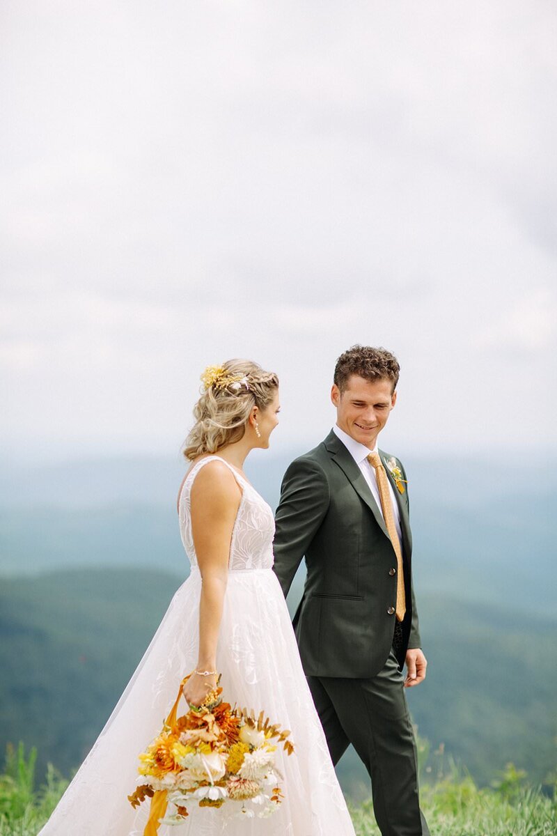 Bride and groom walk hand in hand on the top of a North Carolina mountain