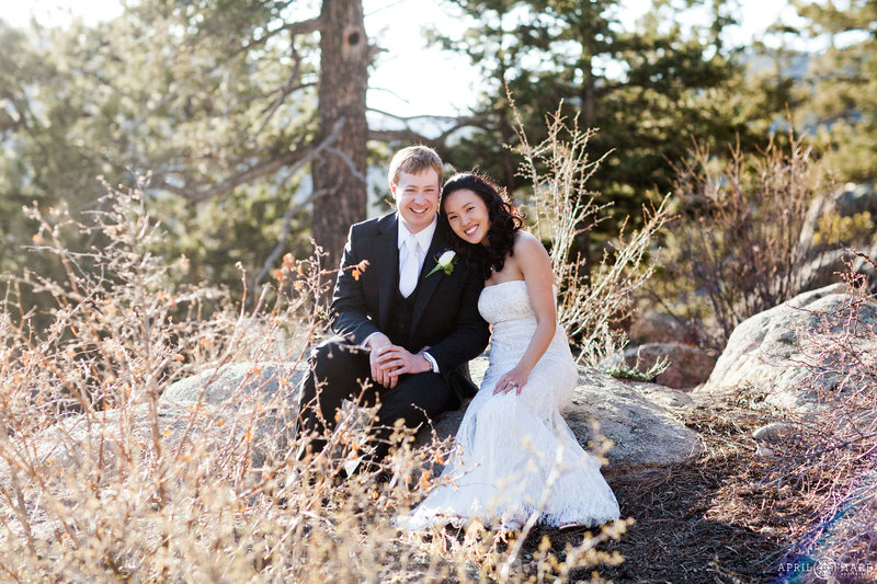 Lovely portrait of a couple seated on rocks in the pretty woods outside of their private VRBO rental home in Estes Park Colorado