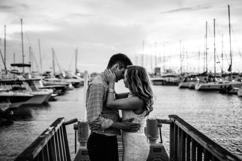 Luxury Portraits by Moving Mountains Photography in NC - Black and white photo of a couple kissing on the dock with boats in the background.