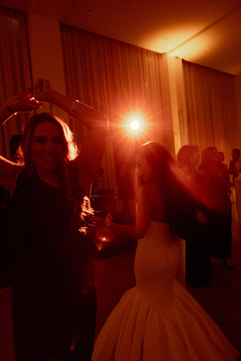 Wedding celebrations at the Dewberry. Bride and wedding guest dancing in red toned light