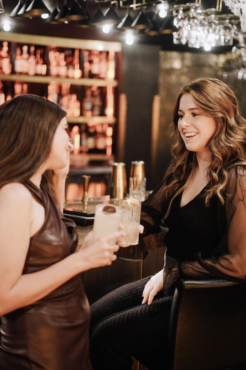 Two women from Knoxville brand agency Liberty Type toast with cocktails at a modern bar with black and gold elements