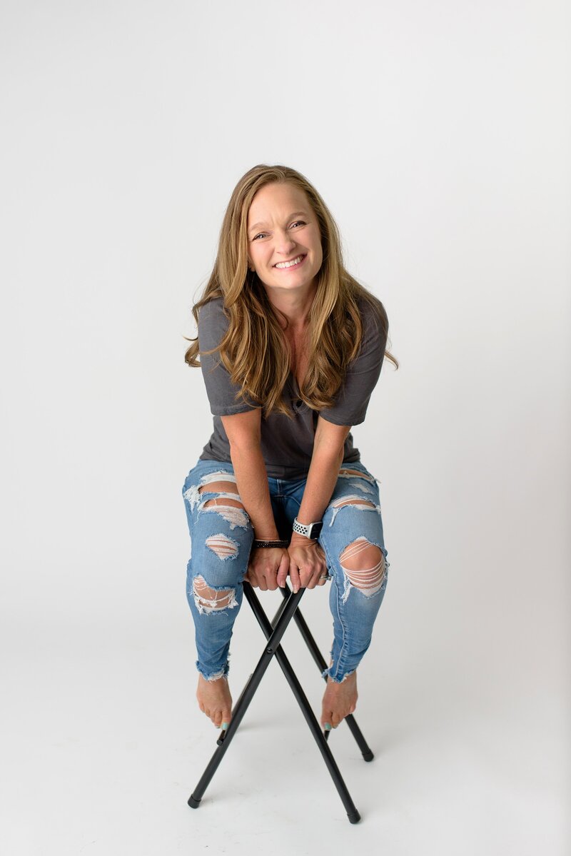 Charlotte Studio photographer sitting on a black stool wearing jeans and a gray t-shirt
