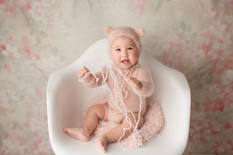 baby girl smiling in a white chair wearing a  pink bear outfit