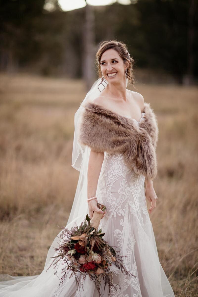 Gorgeous bride wearing faux fur wrap, white lace wedding dress and a bouquet of flowers