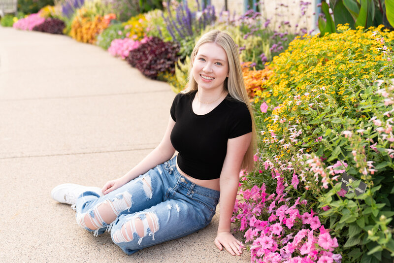 High school girl sits on a sidewalk next to flowers at the Minnesota Landscape Arboretum in Chaska, Minnesota