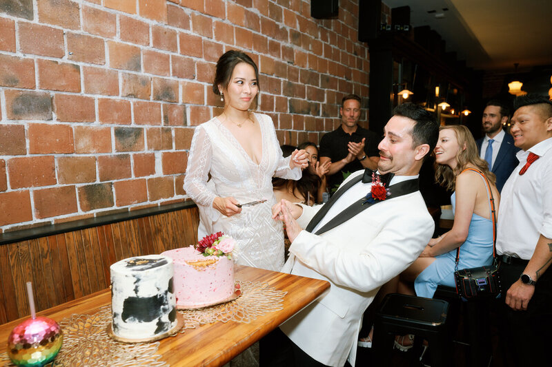 Bride holds the cake cutting knife towards the groom who backs away in mock terror