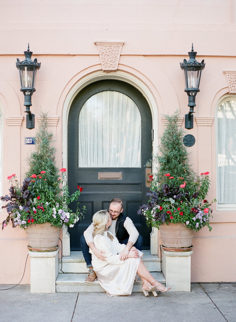 couple takes engagement photos in Charleston on steps, pink building and flowers