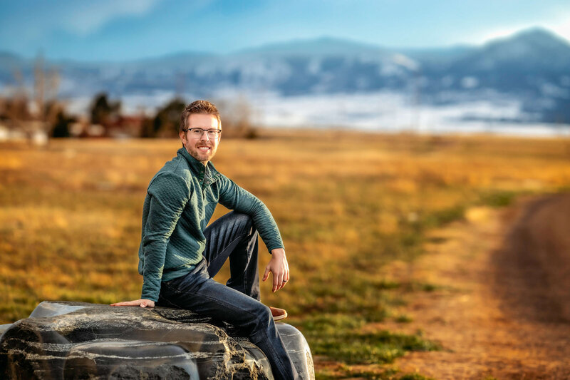 Nick posing on a stone rock in front of the cool Rocky Mountains